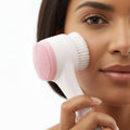 Person using a white and pink facial cleansing brush on a white background